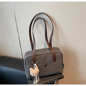 Detail of dark grey canvas tote with brown leather straps and plush bear charm