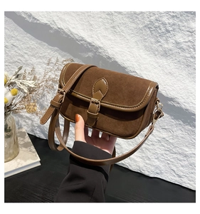 Detail of brown vintage crossbody bag with suede texture and metal buckle on stone backdrop