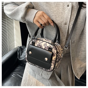 Close-up of beige canvas handbag with dark brown floral prints and black leather straps