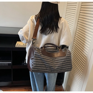Detailed view of grey striped canvas duffel bag with brown leather handles and strap