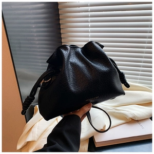 Detail of black pleated cloud bucket bag with knotted handle and gold logo lettering