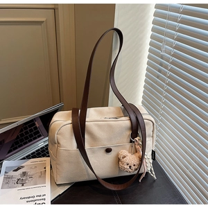 Detail of beige canvas tote bag with brown leather strap and cute bear charm on a desk