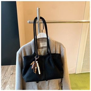Détail d'un sac cabas en daim noir avec breloque en perles de bois sur un blazer kaki