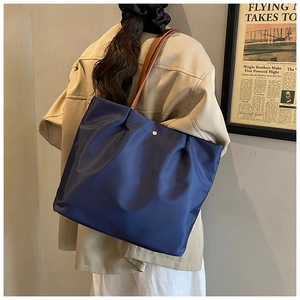 Close-up of blue tote bag with gold snap button, pleat detail and brown leather handle
