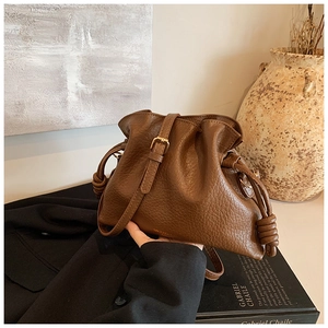 Detail of a dark brown pebble leather drawstring bucket bag with golden logo accents