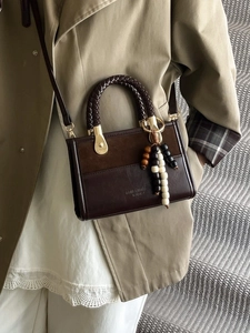 Sac bandoulière marron foncé avec poignée tressée et breloque sur manteau kaki
