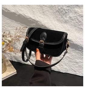 Close-up of black vintage square bag featuring suede texture and gold buckle detail