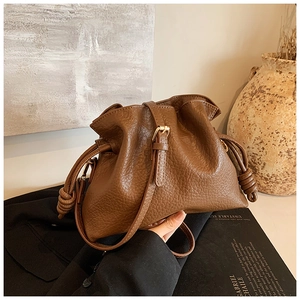 Detail shot of brown lychee texture leather bucket bag with gold hardware and woven knots