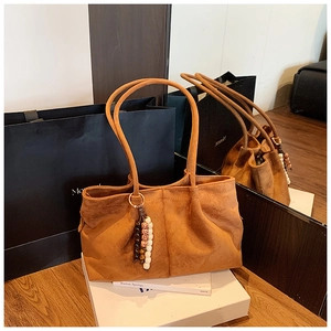 Détail d'un sac cabas en daim marron avec un pendentif en perles décoratif et texture mate