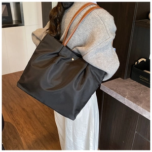 Detail of black nylon tote bag with golden buckle and brown leather shoulder strap