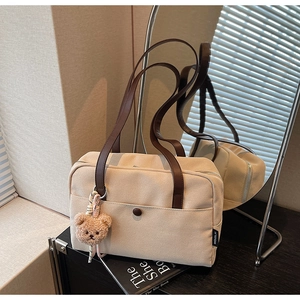 Detail of beige canvas tote bag with brown leather straps and cute plush bear charm