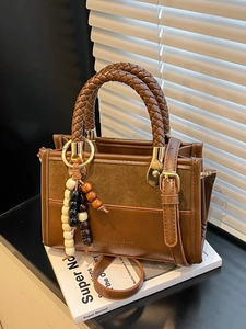Sac bandoulière marron en cuir avec poignée tressée et anneaux sur un livre