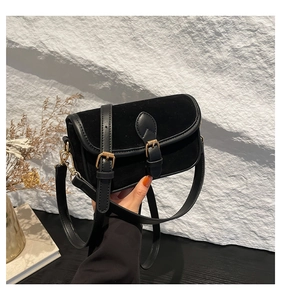 Detailed macro of black suede and smooth leather crossbody bag with gold buckle hardware