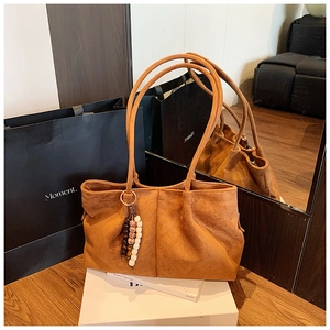 Détail d'un sac cabas en daim marron avec bandoulière et pendentif décoratif en perles