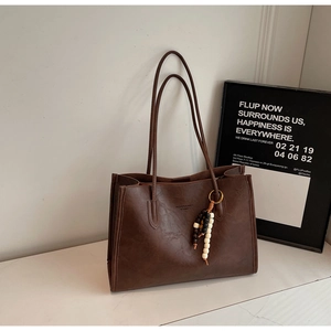 Detail of dark brown leather tote bag with lychee texture and wooden bead tassel