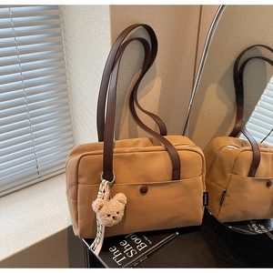 Detail of khaki canvas tote bag with leather straps and cute plush bear charm