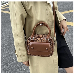 Retro brown leather floral handbag worn with a beige trench coat on a street