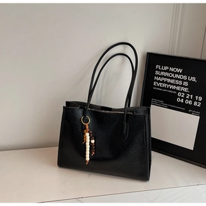 Detail of black faux leather tote bag with glossy texture and beaded charm accessory