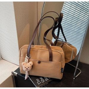 Detail of khaki canvas tote bag featuring brown leather handles and a plush bear charm