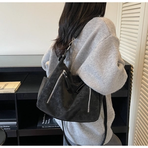 Detail of black suede tote bag with dual silver zippers shown on a grey sweater