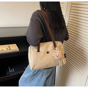 Detail shot of beige canvas tote bag with dark brown straps and cute bear charm pendant