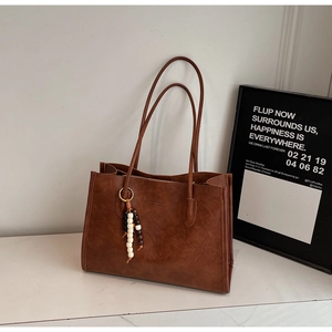 Detail of dark brown vintage tote bag with fashion embossing and wooden bead tassel