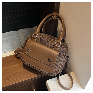 Detail of vintage brown paisley satchel with leather flap and adjustable strap on a wood desk