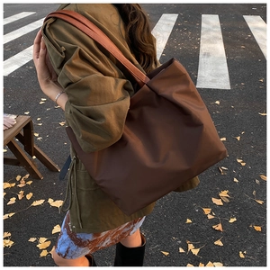 Detail of a dark brown nylon tote bag with leather straps on a sidewalk setting