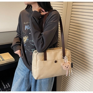 Detail of beige canvas tote with brown straps and cute bear charm shown on model