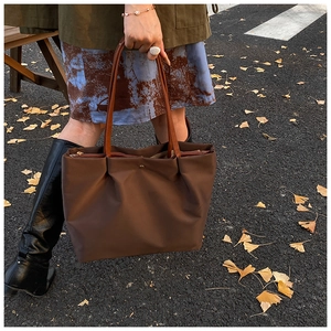 Detail of a dark brown large tote bag with pleated design and metallic clasp for autumn