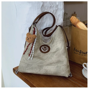 Détail du sac hobo vert sauge avec logo M en métal et charm d'ours en peluche brun