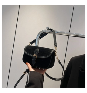 Detail of vintage black suede crossbody bag featuring gold buckle and leather trim finish