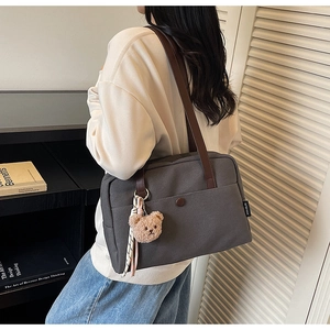 Detail of dark grey canvas tote bag with brown leather straps and cute plush bear charm