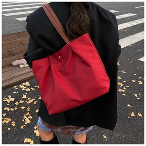 Red tote bag with golden buckle and brown straps shown in an autumn street scene