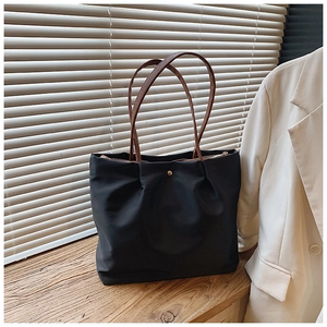 Detail view of large black tote bag with brown faux leather straps and golden hardware