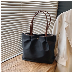Close-up of ruched black tote bag with brown leather straps and golden metal zipper