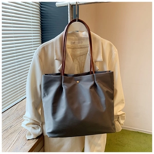 Detail of dark grey tote bag featuring premium gold snap button and brown leather handle