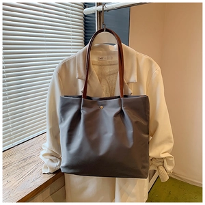 Detail of grey nylon tote bag with leather handles and gold snap button on a blazer