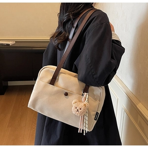 Detail of off-white canvas tote bag with brown leather straps and plush bear charm