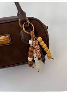 Détail du sac Boston en daim marron vintage avec plaque dorée et perles en bois colorées
