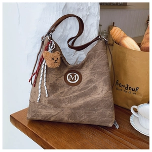 Détail du sac hobo en toile marron avec logo M en cuir et breloque ours peluche
