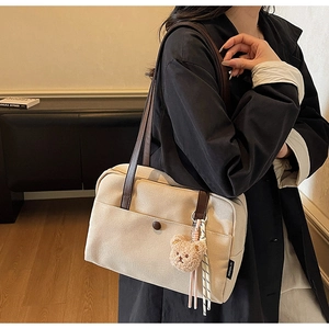 Detail shot of beige canvas tote bag with brown leather strap and plush bear charm