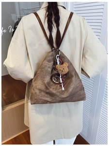 Détail d'un sac à dos vintage marron avec logo M argenté et breloque ours en peluche