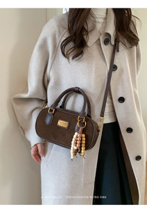 Détail du sac cylindrique en daim marron avec perles en bois et plaque logo dorée