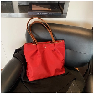 Red nylon tote bag on a black leather chair featuring brown straps and a gold zipper