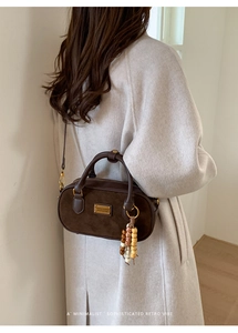 Détail du sac à bandoulière café noir avec pendentif en bois et logo en métal épuré