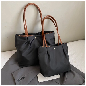 Detail of nylon tote bag set with brown leather handles and golden metal hardware