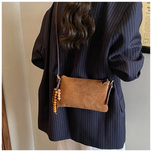 Bolso bandolera de ante marrón con borla de madera mostrado sobre una modelo