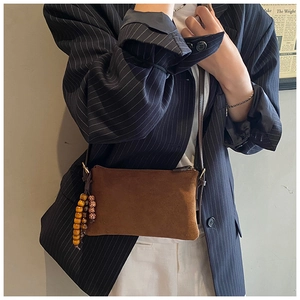 Detalle de bolso bandolera de ante marrón con colgante étnico de cuentas de madera