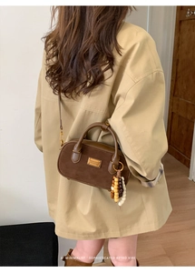 Gros plan d'un sac à main rétro en daim marron avec pampille et logo doré sur trench